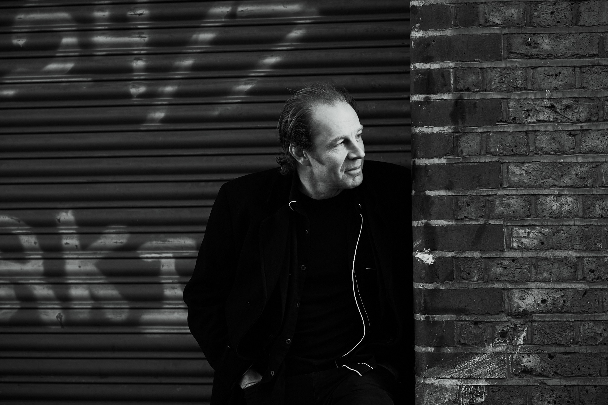 Mid shot of Charlie James leaning on the wall, smiling and looking to the left in black and white